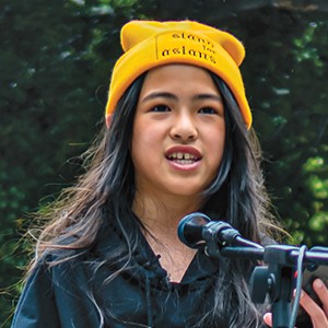 A girl wearing a yellow beanie speaking into a podium microphone
