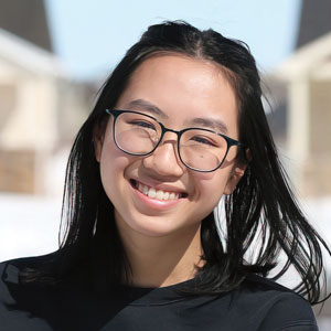 A young woman wearing black glasses and smiling brightly