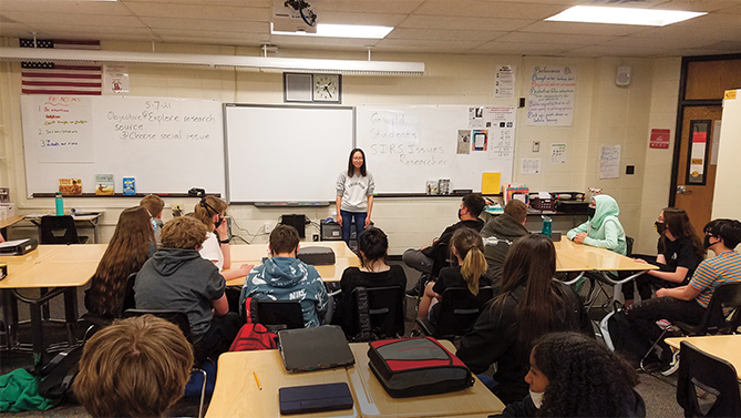 Enlargeable photo of a young woman speaking in front of a class of other teens