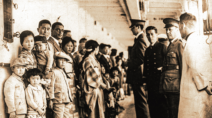Black and white photo of Chinese immigrant families lined up against a wall