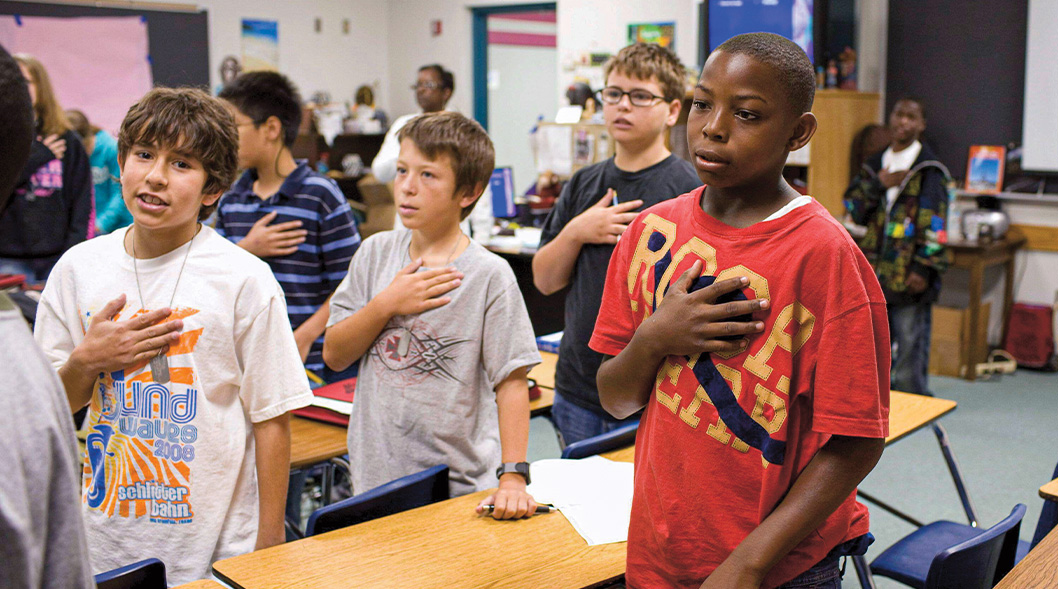 Students in class standing up and saying the Pledge of Allegiance