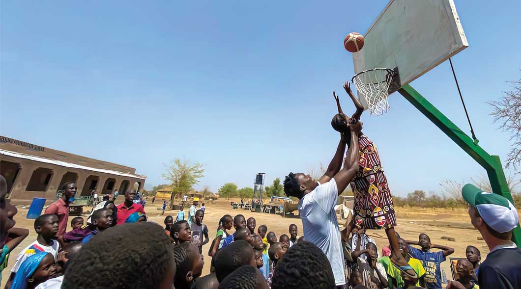 Photo of an adult helping little kids score a hoop in basketball