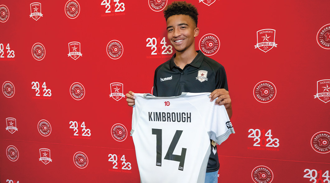 Photo of a teen professional soccer player smiling & holding their new uniform