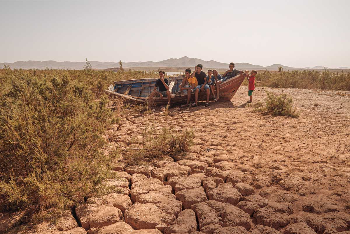 Photo of kids sitting in an abandoned boat located in a dried up lake