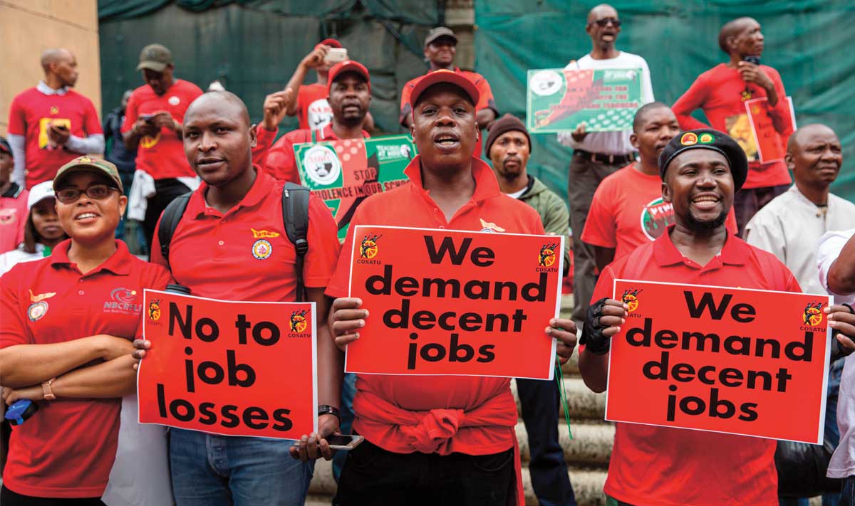 Photo of people protesting with signs like, "We demand decent jobs"