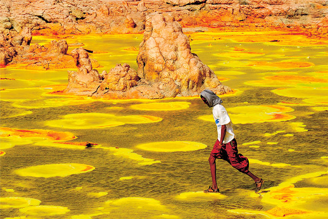 Enlargeable photo of a person walking on mineral deposits to avoid yellowish-green toxic water